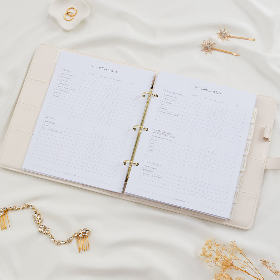 Open wedding planner binder showing a detailed wedding budget tracker spread covering bride, groom, bridesmaids and rings