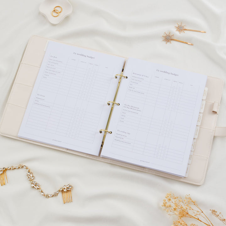 Open wedding planner binder showing a detailed wedding budget tracker spread covering bride, groom, bridesmaids and rings