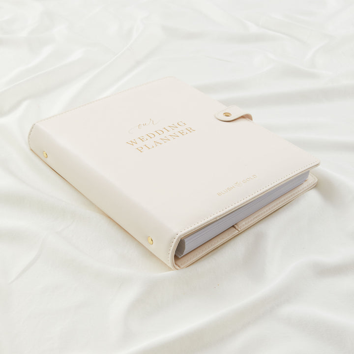 Cream leather wedding planner binder with gold foil text closed on white silk