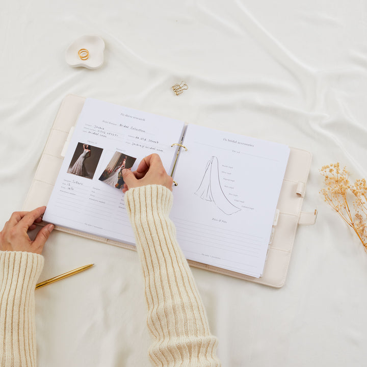 Hands adding dress inspiration photos to a filled-in wedding planner binder dress research page alongside a bridal veil accessories diagram
