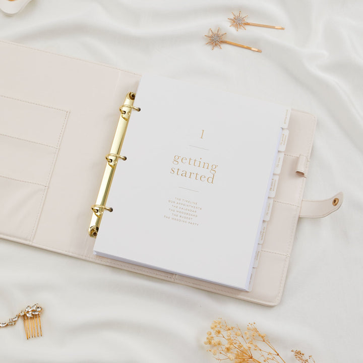 Open wedding planner binder showing the getting started section divider with gold foil text and interior pocket pages visible on the left