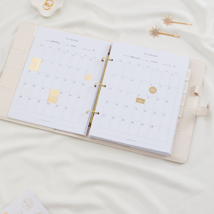 Hand placing a gold foil sticker onto a wedding planner calendar page with countdown sticker sheets laid out nearby
