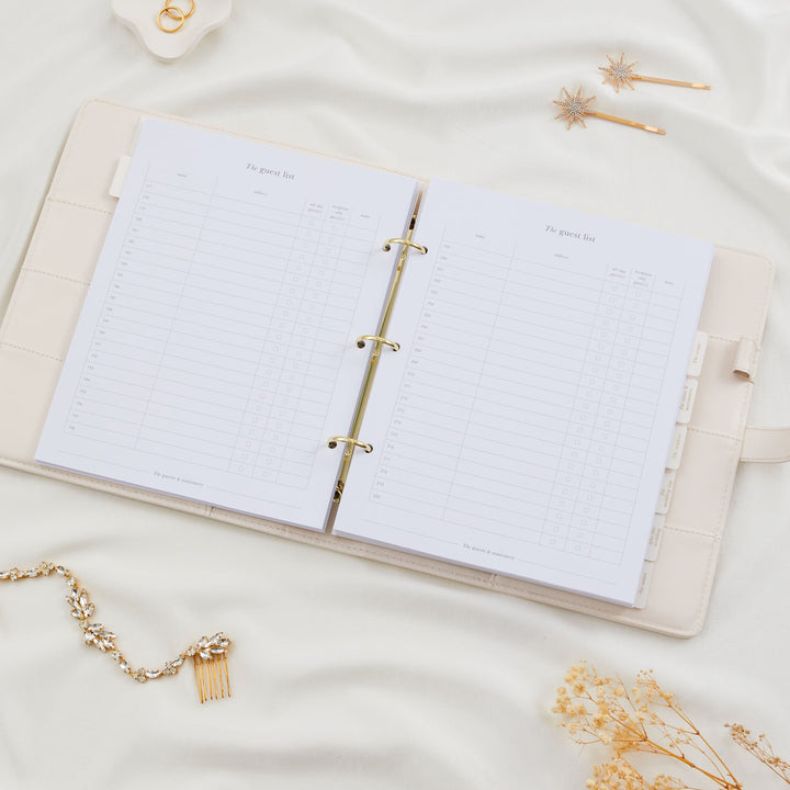 Open wedding planner binder showing a double page guest list spread with numbered rows for up to 220 guests styled on a cream silk background with bridal accessories