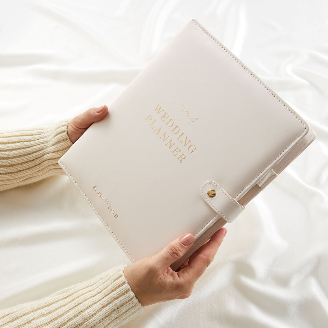 Woman holding cream wedding planner binder with gold foil cover