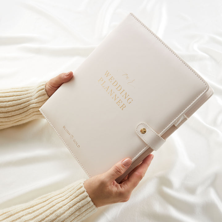 Woman holding cream wedding planner binder with gold foil cover