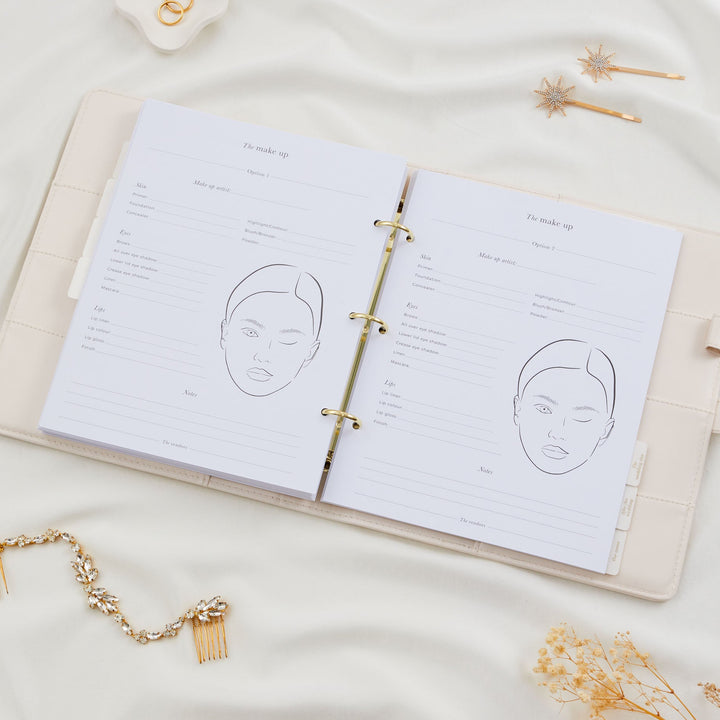 Open wedding planner binder showing two bridal makeup planning pages with face chart line illustrations and product fields for skin, eyes and lips with gold foil tabs visible