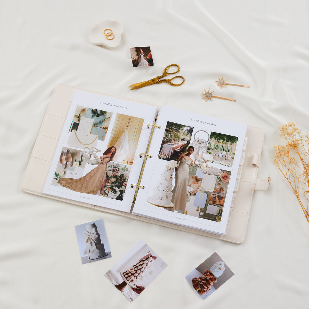 Open wedding planner binder showing filled moodboard pages with bridal inspiration photos surrounded by loose photos and gold scissors