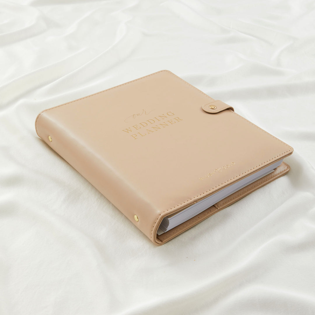 Closed nude leather wedding planner binder by Blush and Gold showing spine thickness and gold stud detailing on white linen