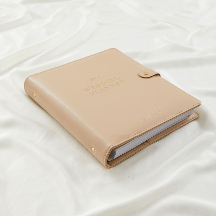 Closed nude leather wedding planner binder by Blush and Gold showing spine thickness and gold stud detailing on white linen