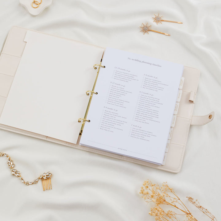 Open wedding planner binder showing a full wedding planning timeline checklist from 12 months to one week before the wedding day