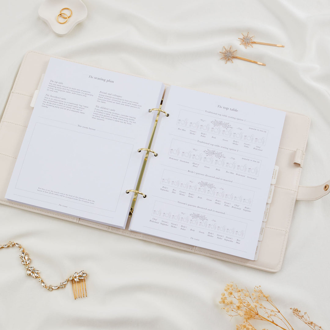 Open wedding planner binder showing seating plan guidance and top table layout diagrams including traditional and divorced parent arrangements styled with bridal accessories