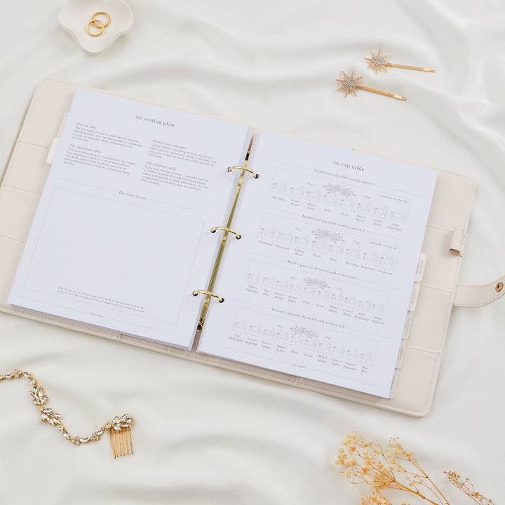 Open wedding planner binder showing seating plan guidance and top table layout diagrams including traditional and divorced parent arrangements styled with bridal accessories