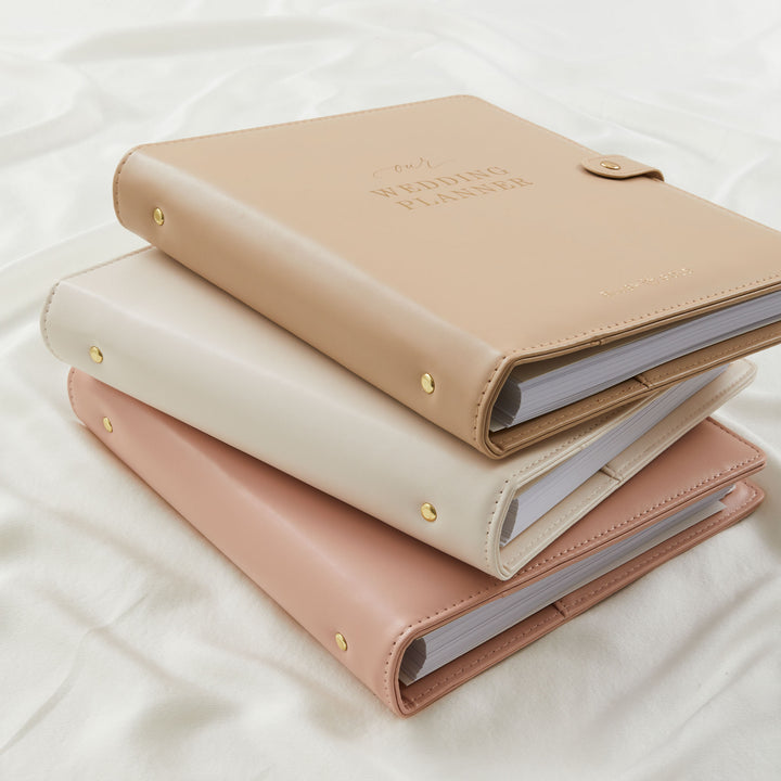 Wedding planner binders in tan, cream and blush stacked on white fabric