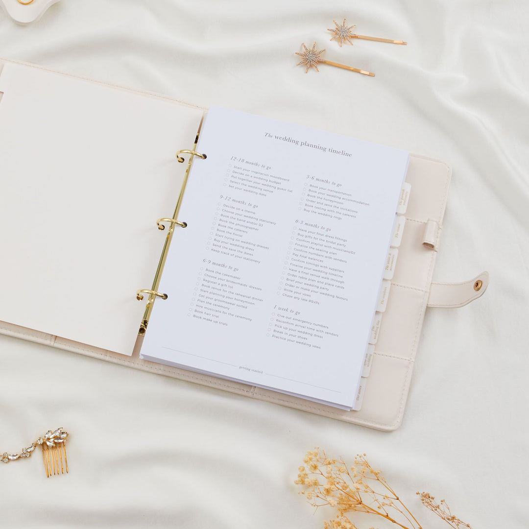 Open wedding planner binder showing a wedding planning timeline checklist with tasks from 12 months to one week before the wedding