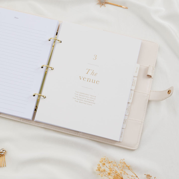 Open wedding planner binder showing section three titled The Venue with gold ring binder and tabbed dividers